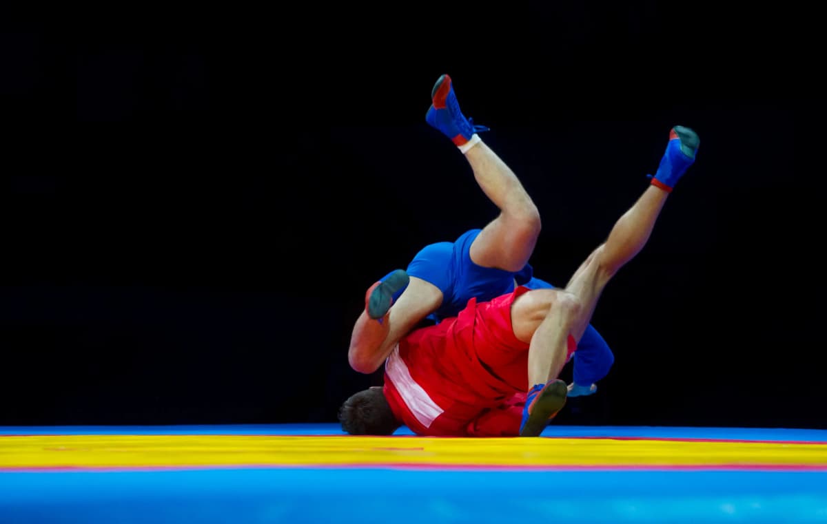 Twee sambo-sporters in een rode en een blauwe kurtka tijdens een worp op de wedstrijdmat